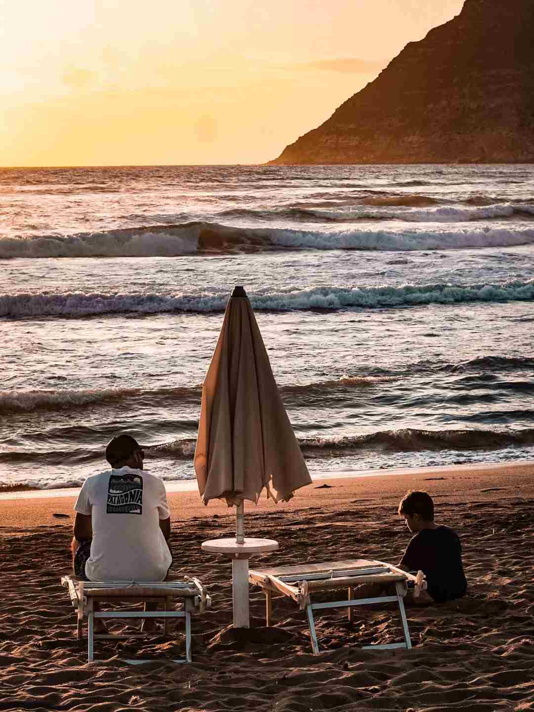 Uomo e bambino seduti sulla spiaggia di Porto Ferro al tramonto
